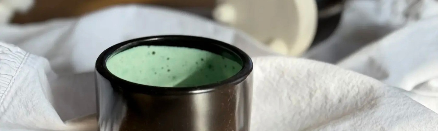 A black ceramic cup with a mint-colored interior, placed on a wooden table with a white napkin in the background. Another overturned cup is visible in the background.