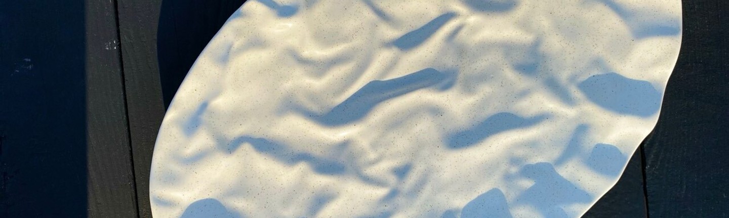 Ceramic oval plate in white with a textured surface, placed on a dark background.